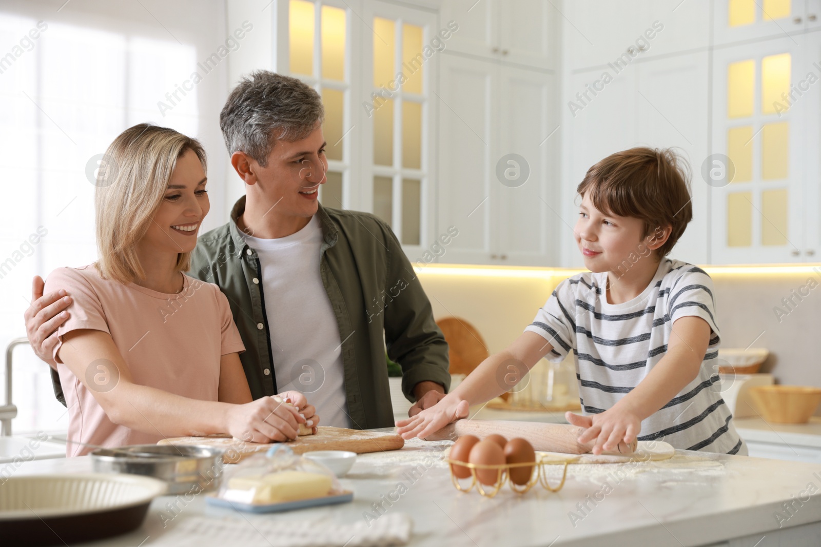 Photo of Happy family kneading dough at white marble table in kitchen