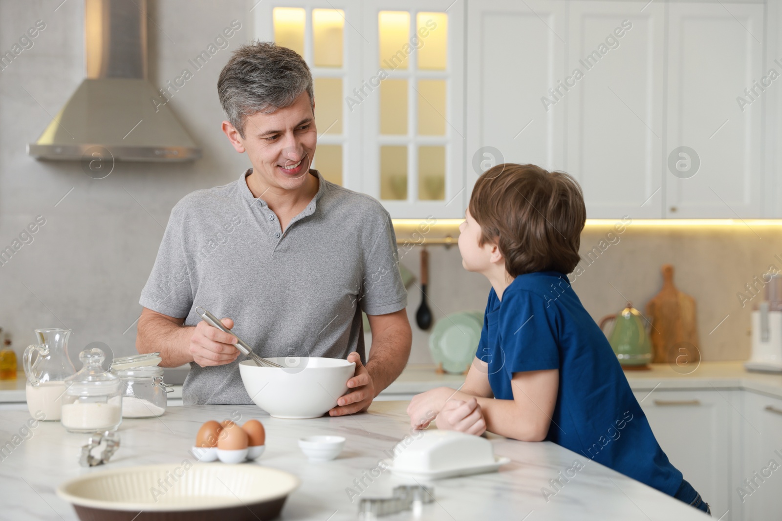 Photo of Father and his son making dough at white marble table in kitchen