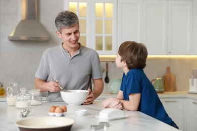 Photo of Father and his son making dough at white marble table in kitchen