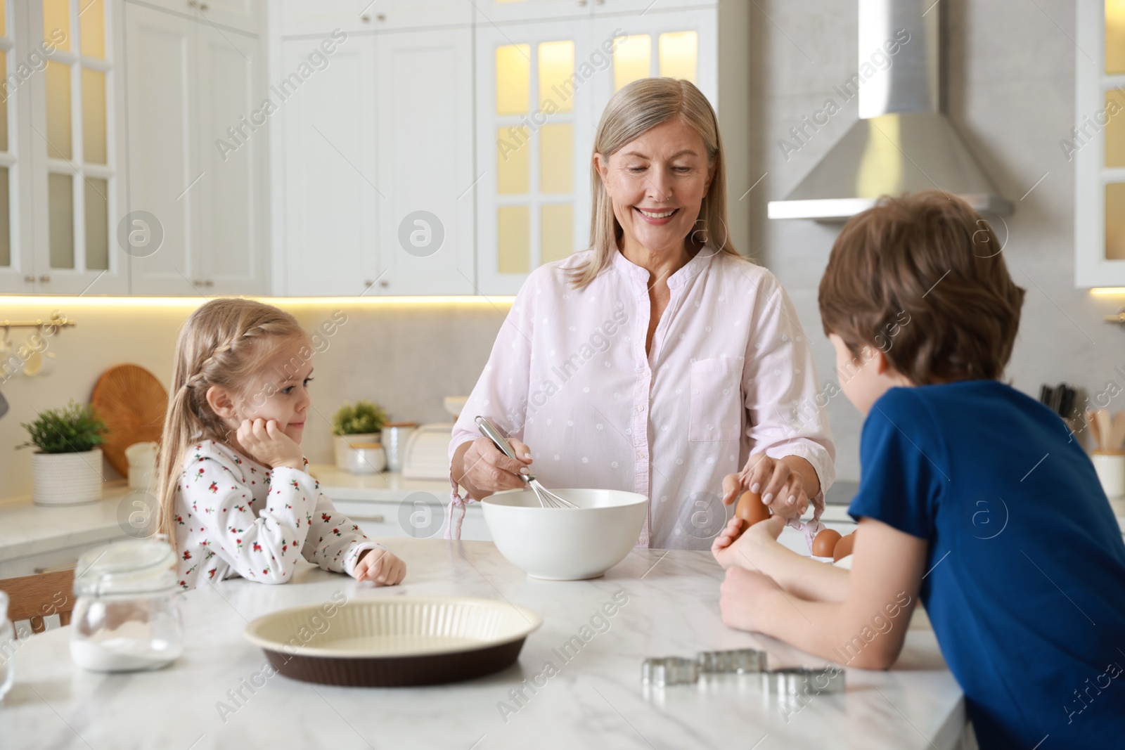 Photo of Grandmother and her grandchildren making dough at white marble table in kitchen