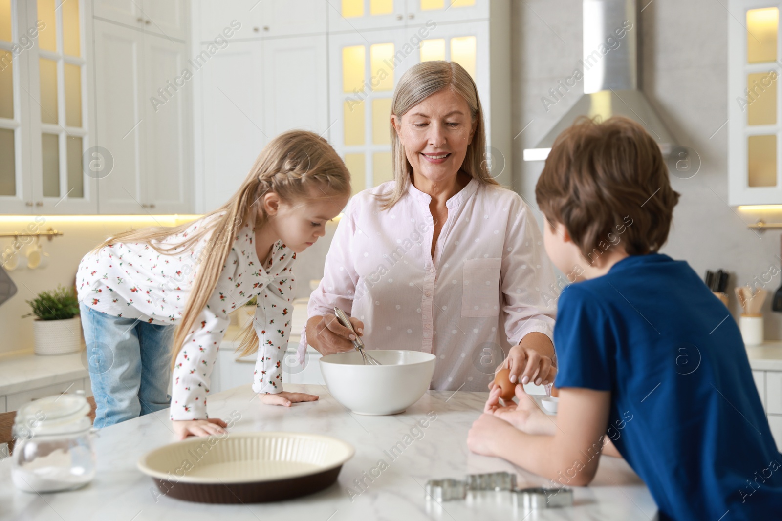 Photo of Grandmother and her grandchildren making dough at white marble table in kitchen