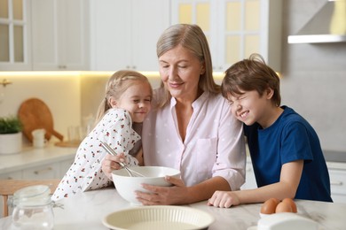 Photo of Grandmother and her grandchildren making dough at white marble table in kitchen