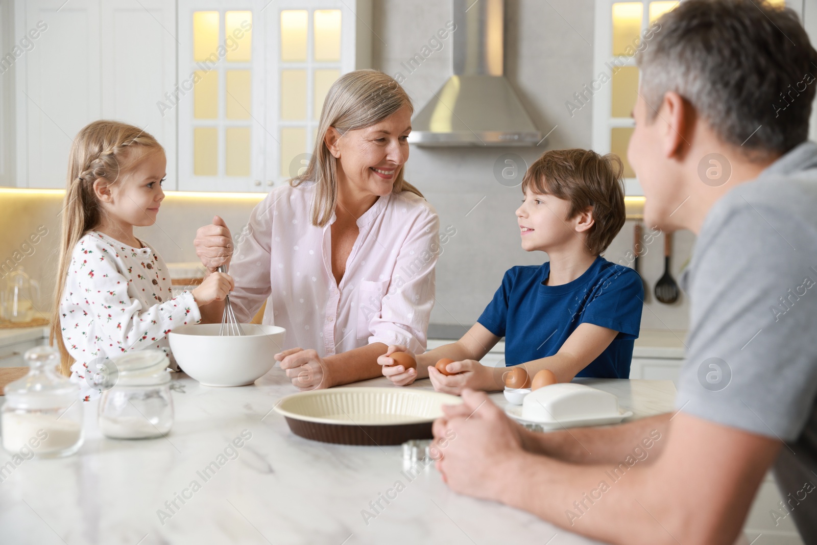 Photo of Little kids with their father and grandmother making dough at marble table in kitchen