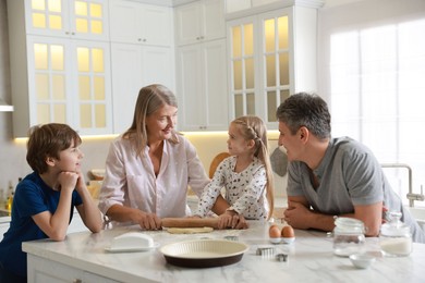 Photo of Little kids with their father and grandmother making dough at marble table in kitchen