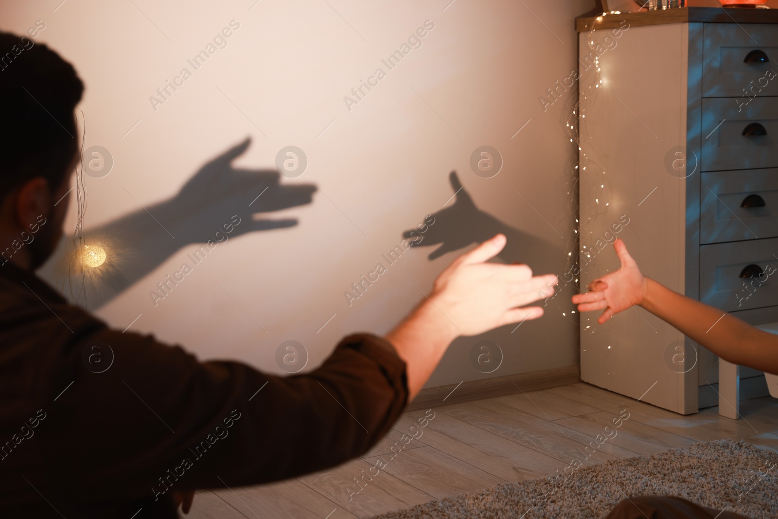 Photo of Shadow play. Father and his son making hand gestures like dogs on wall at home, closeup