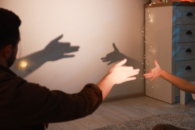 Photo of Shadow play. Father and his son making hand gestures like dogs on wall at home, closeup