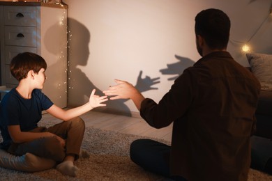 Photo of Shadow play. Father and his son making hand gestures like dogs on wall at home