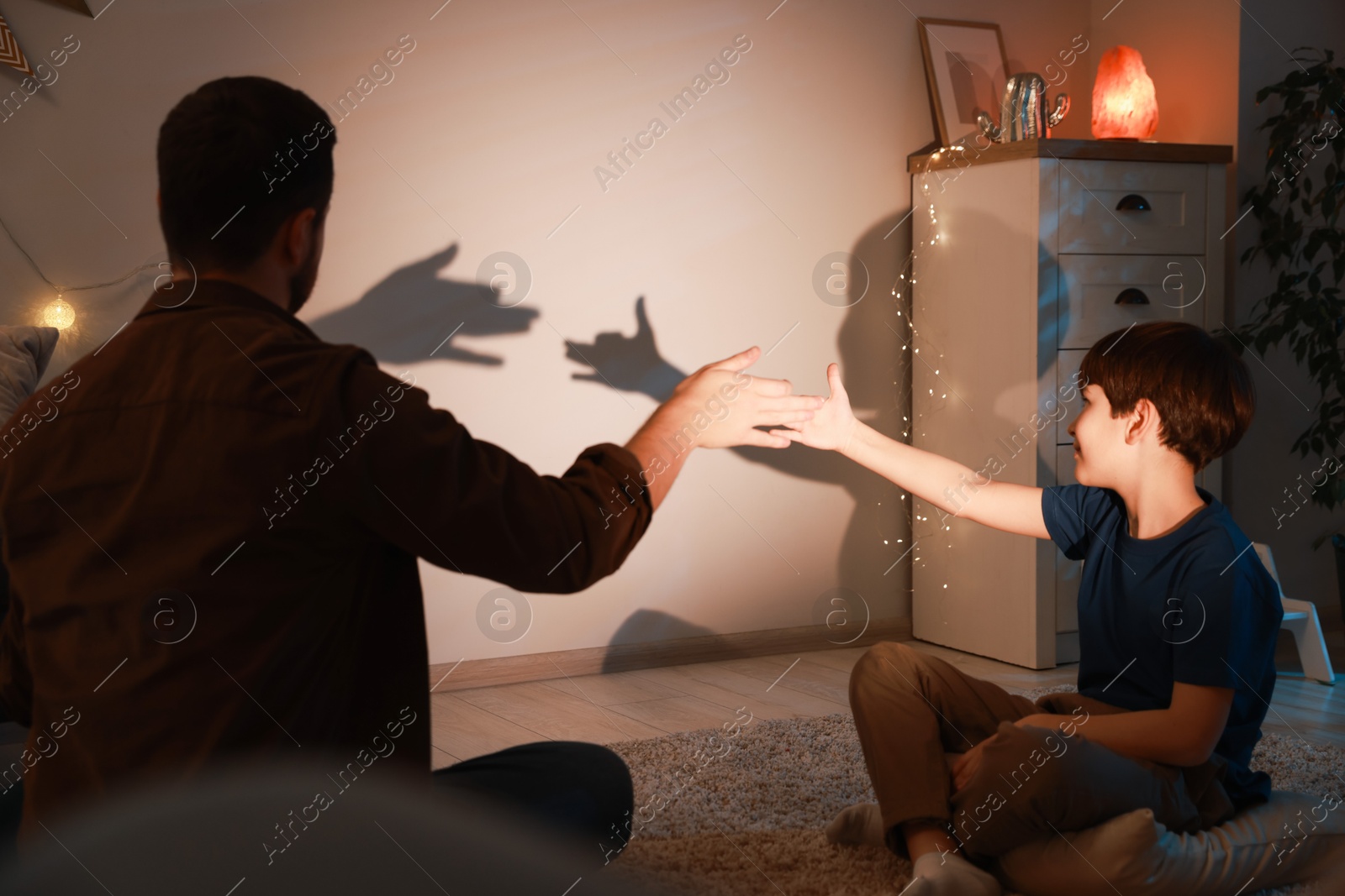 Photo of Shadow play. Father and his son making hand gestures like dogs on wall at home