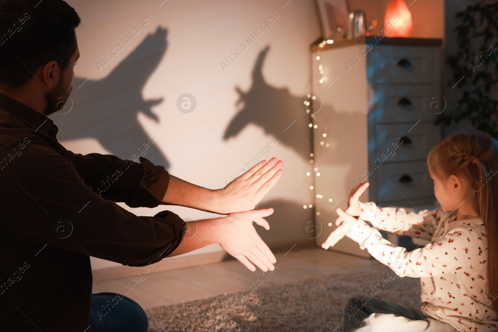 Photo of Shadow play. Father and his daughter making hand gestures like birds on wall at home