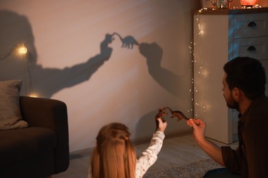 Photo of Father and his daughter performing shadow play with toy dinosaurs at home