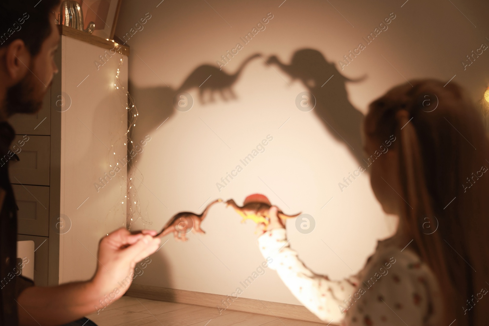 Photo of Father and his daughter performing shadow play with toy dinosaurs at home, closeup