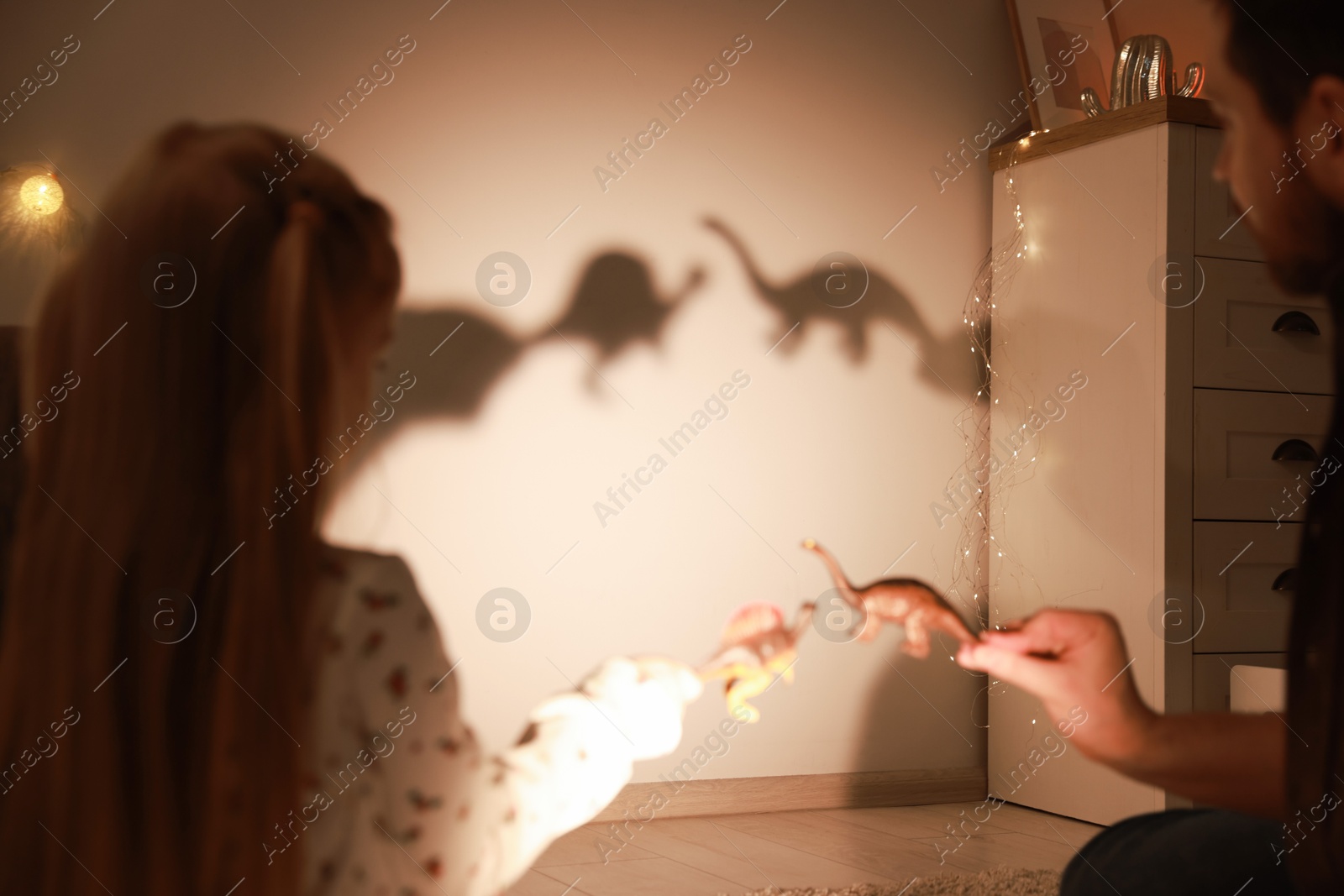 Photo of Father and his daughter performing shadow play with toy dinosaurs at home, closeup