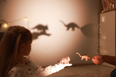 Photo of Father and his daughter performing shadow play with toy dinosaurs at home, closeup