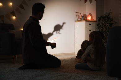 Photo of Father performing shadow play with toy dinosaur to his kids at home