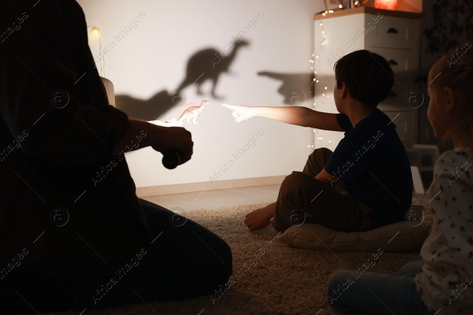 Photo of Father performing shadow play with toy dinosaur to his kids at home, closeup