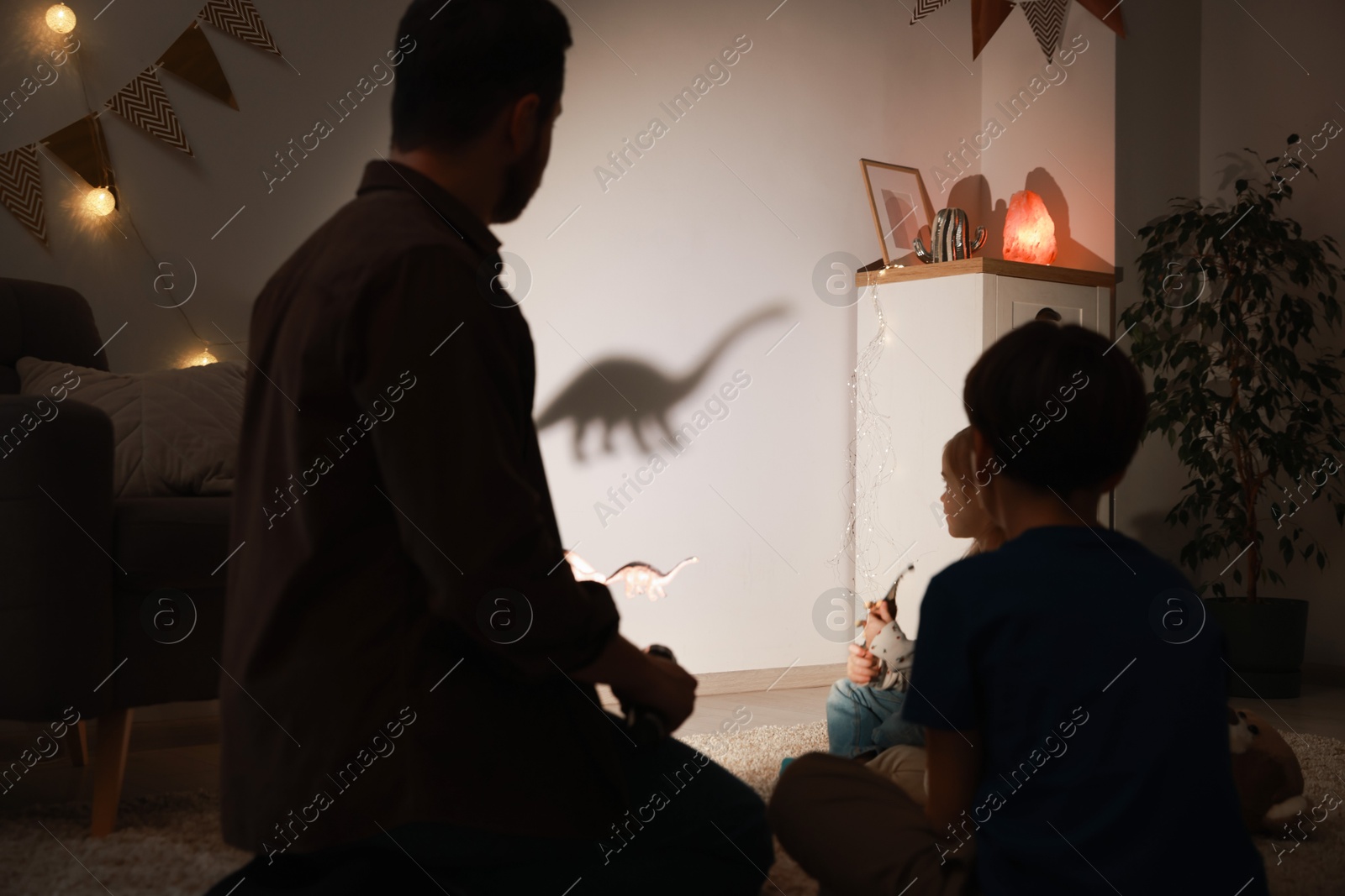 Photo of Father performing shadow play with toy dinosaur to his kids at home