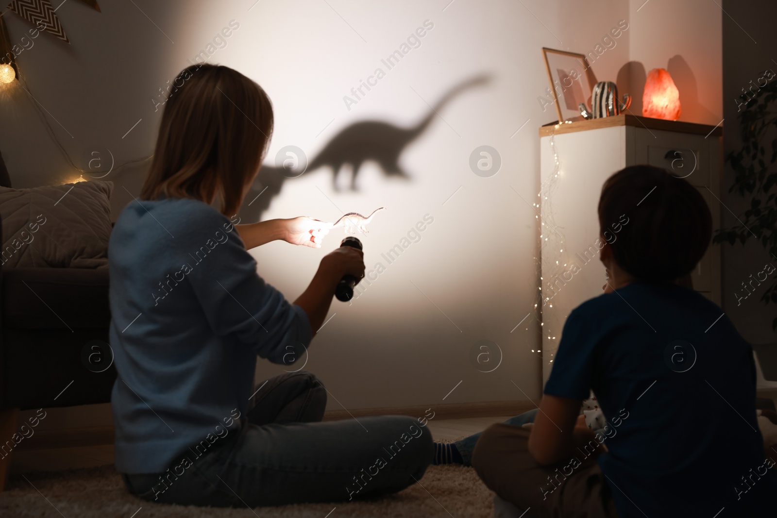 Photo of Mother performing shadow play with toy dinosaur to her kids at home