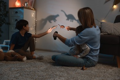 Photo of Mother and her son performing shadow play with toy dinosaurs at home