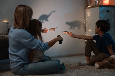 Photo of Mother and her son performing shadow play with toy dinosaurs at home