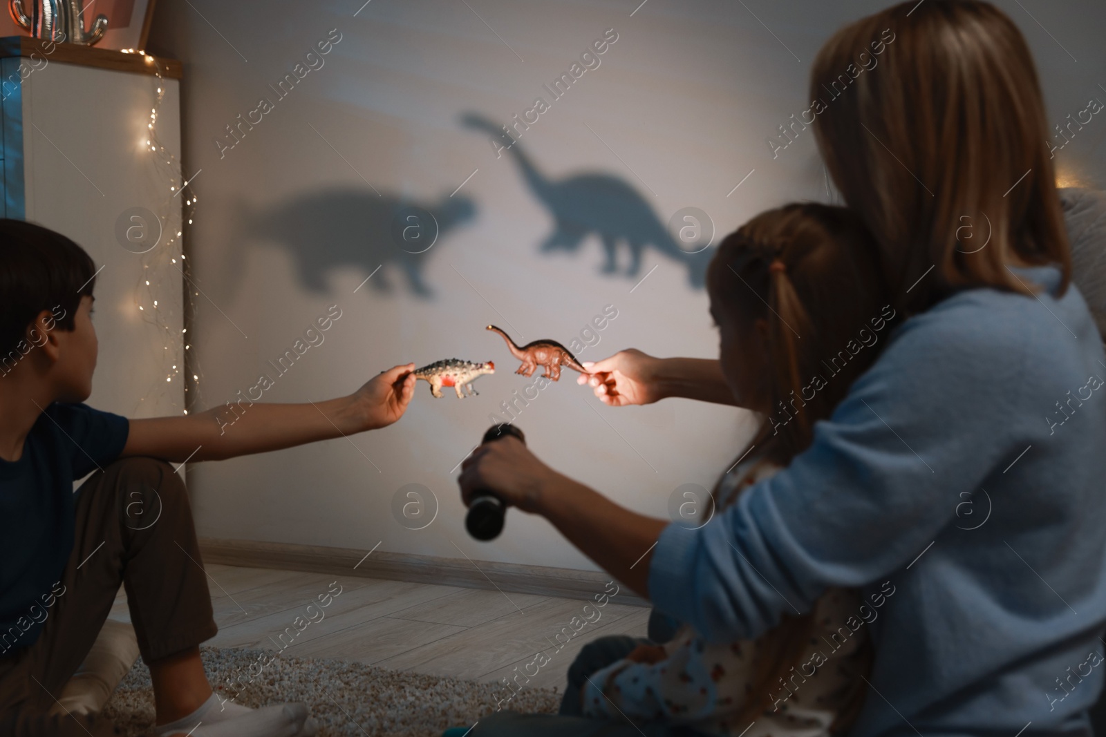 Photo of Mother and her son performing shadow play with toy dinosaurs at home