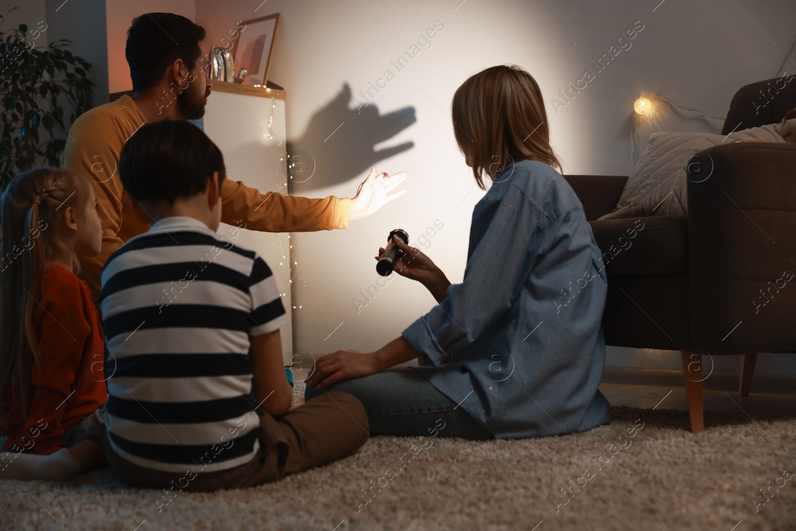 Photo of Man making hand gesture like dog while performing shadow play to his family at home