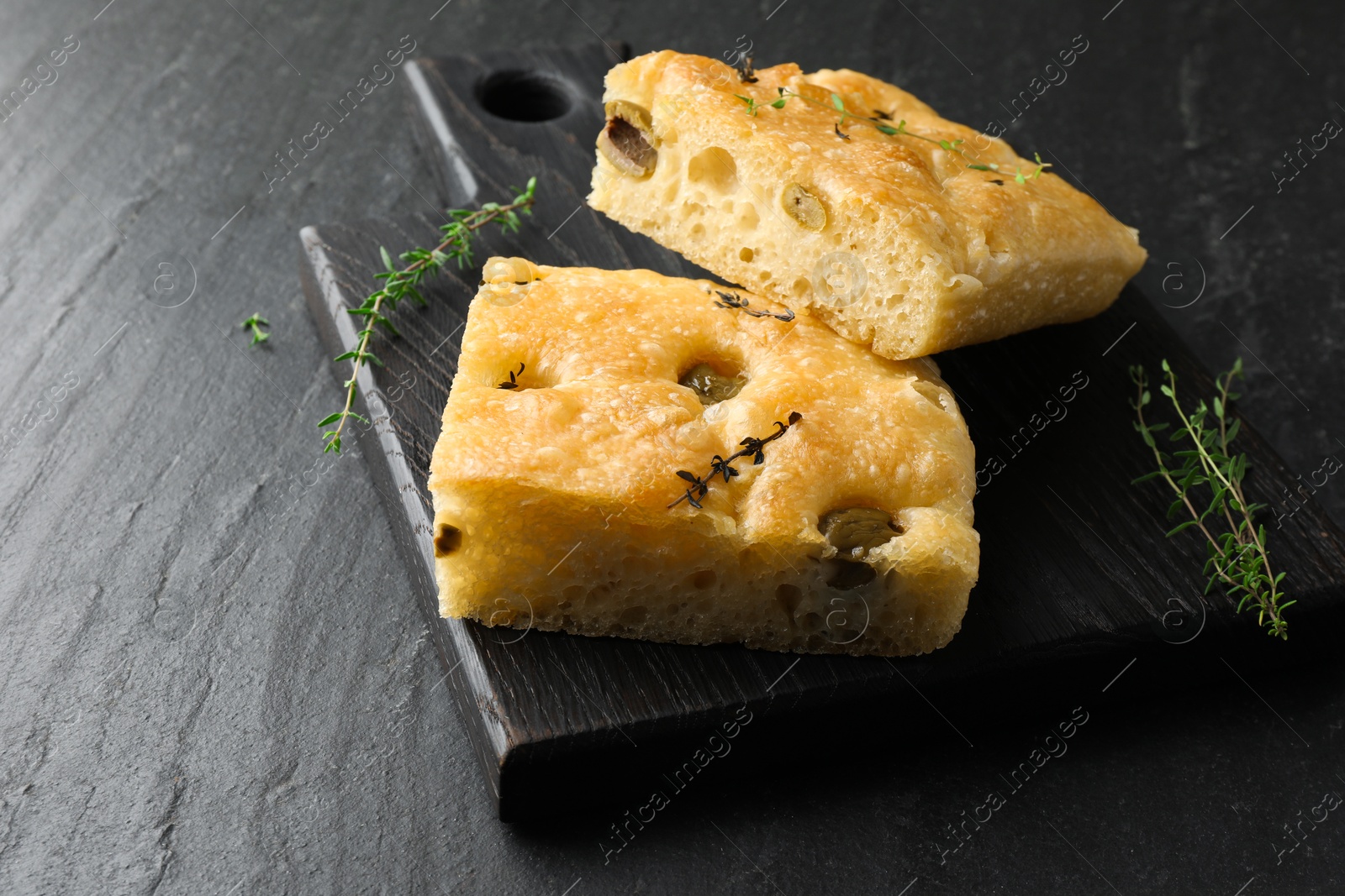 Pieces of delicious focaccia bread with olives and thyme on black table, closeup. Space for text Photo of Pieces of delicious focaccia bread with olives and thyme on black table, closeup. Space for text