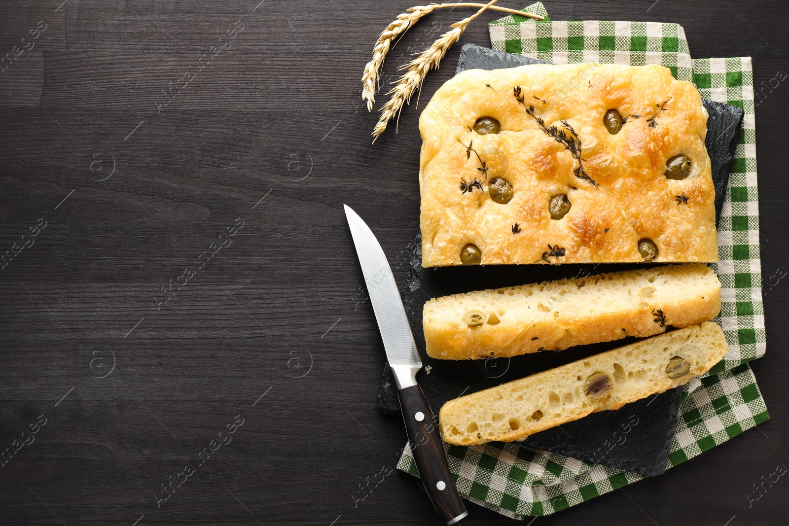 Pieces of delicious focaccia bread with olives, thyme, spikes and knife on dark wooden table, flat lay. Space for text Photo of Pieces of delicious focaccia bread with olives, thyme, spikes and knife on dark wooden table, flat lay. Space for text