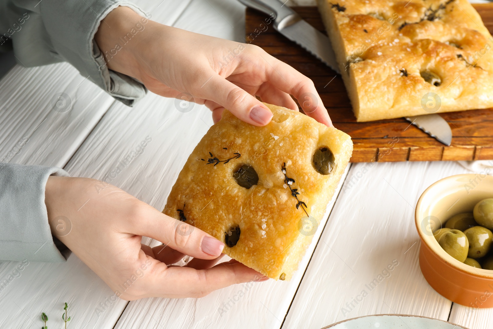 Woman with piece of delicious focaccia bread at white wooden table, closeup Photo of Woman with piece of delicious focaccia bread at white wooden table, closeup