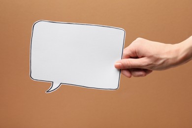 Photo of Woman holding blank speech bubble on brown background, closeup. Space for text