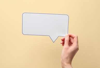 Photo of Woman holding blank speech bubble on beige background, closeup. Space for text