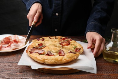 Photo of Woman cutting delicious focaccia bread at wooden table, closeup