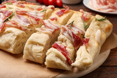 Photo of Slices of delicious focaccia bread with bacon and rosemary on wooden table, closeup