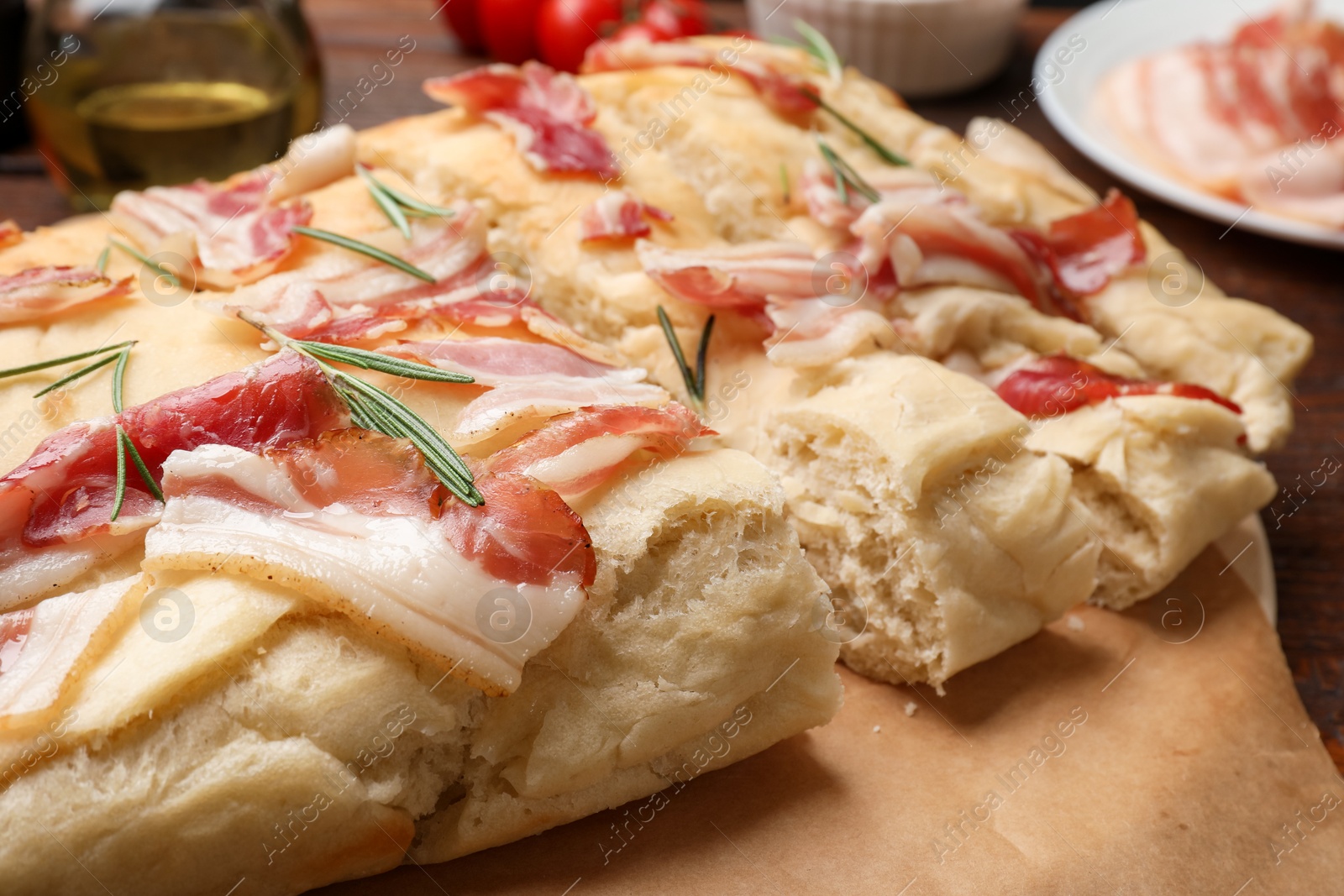 Photo of Slices of delicious focaccia bread with bacon and rosemary on table, closeup