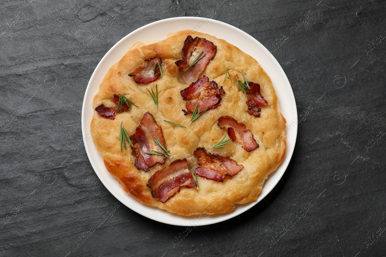 Photo of Delicious focaccia bread with bacon and rosemary on black table, top view