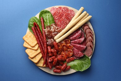 Photo of Different smoked sausages and other snacks on blue background, top view