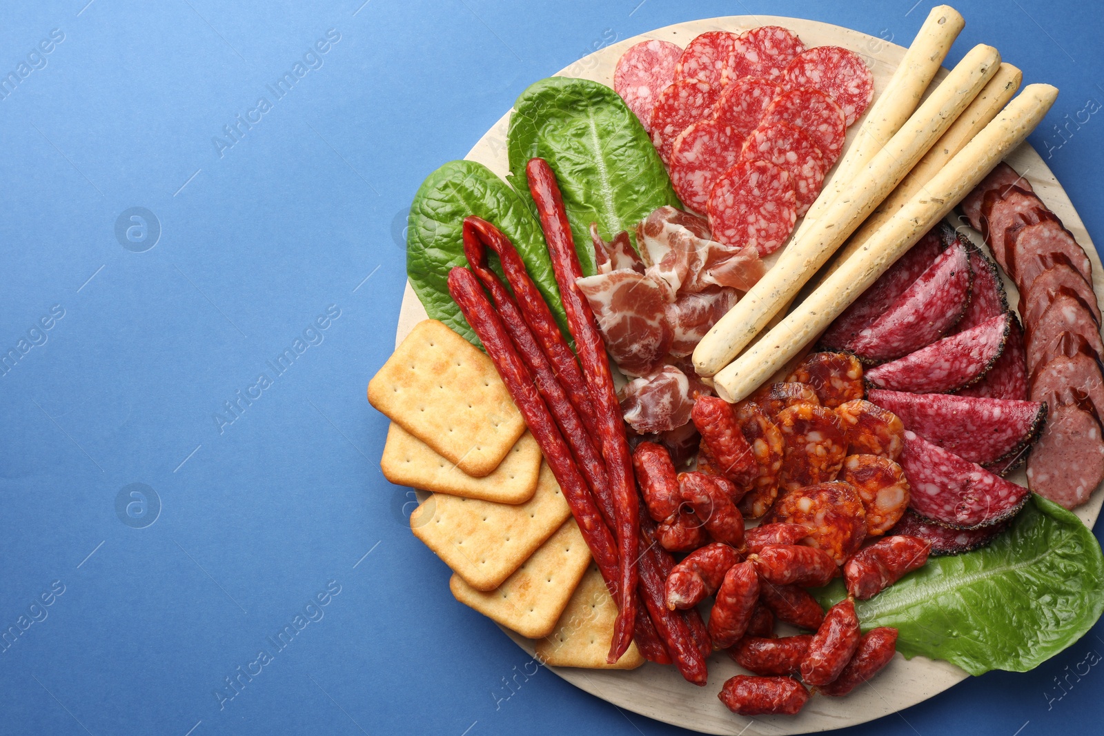 Photo of Different smoked sausages and other snacks on blue background, top view. Space for text