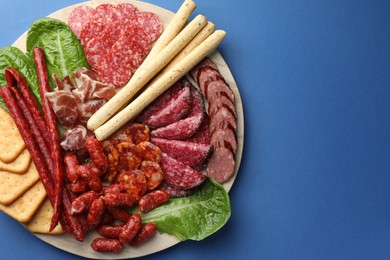 Photo of Different smoked sausages and other snacks on blue background, top view. Space for text