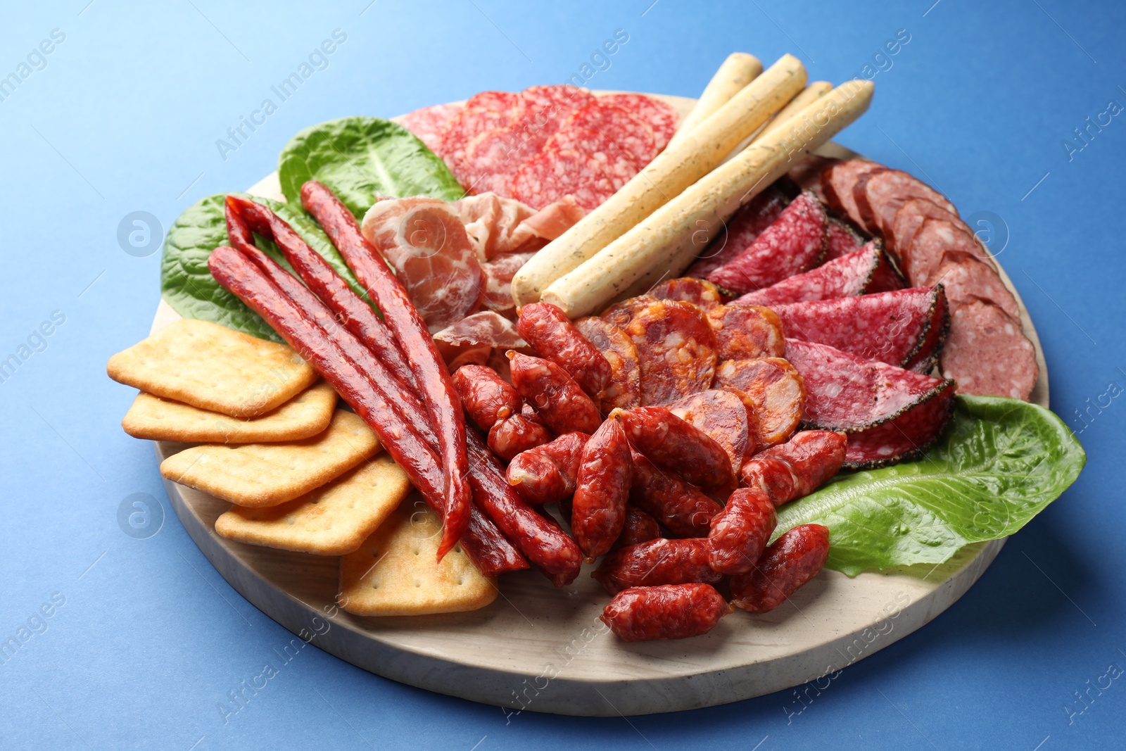 Photo of Different smoked sausages and other snacks on blue background, closeup