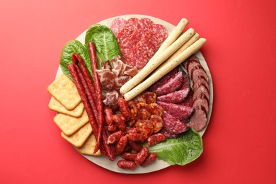 Photo of Different smoked sausages and other snacks on red background, top view