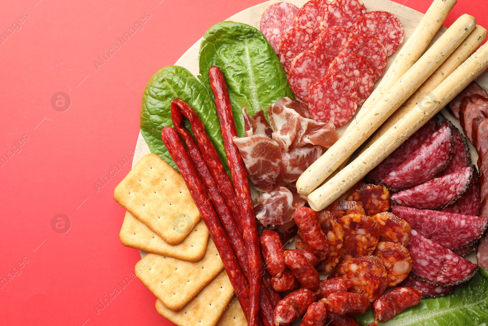 Photo of Different smoked sausages and other snacks on red background, top view. Space for text