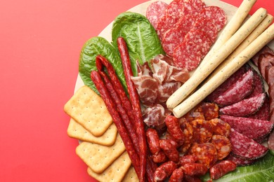 Photo of Different smoked sausages and other snacks on red background, top view. Space for text