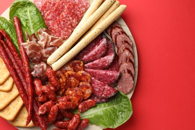 Photo of Different smoked sausages and other snacks on red background, top view. Space for text