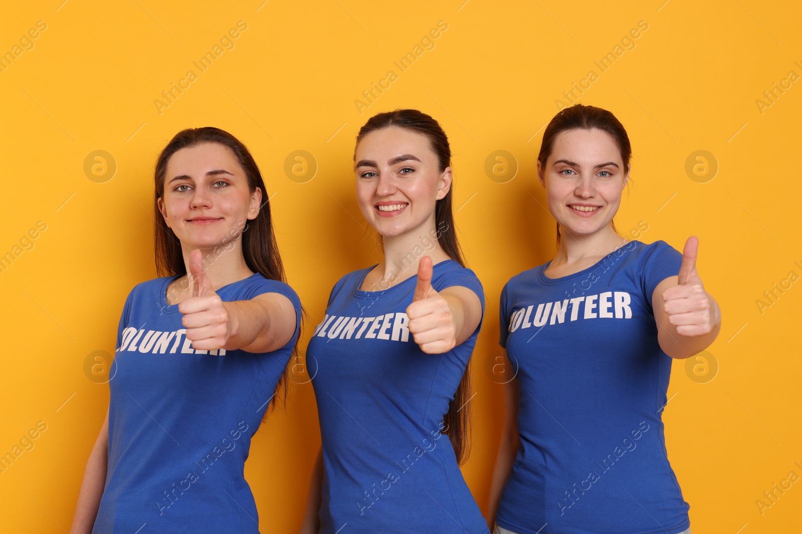 Photo of Team of volunteers showing thumbs up on orange background