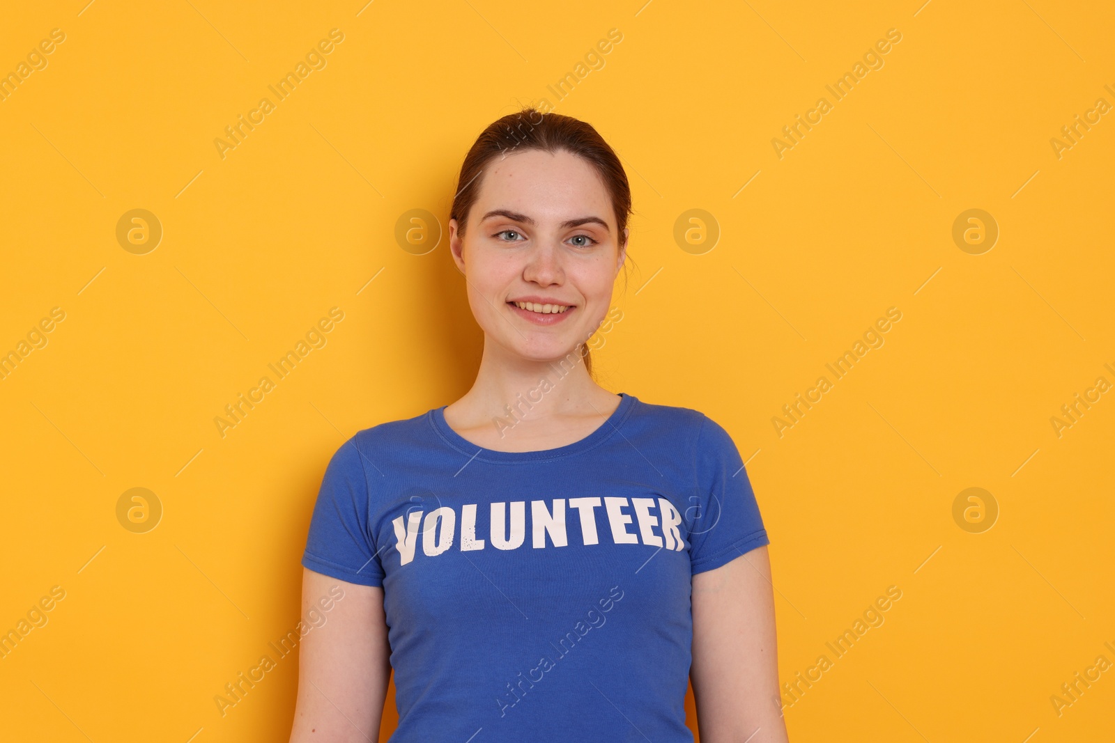 Photo of Portrait of smiling woman in t-shirt with word Volunteer on orange background