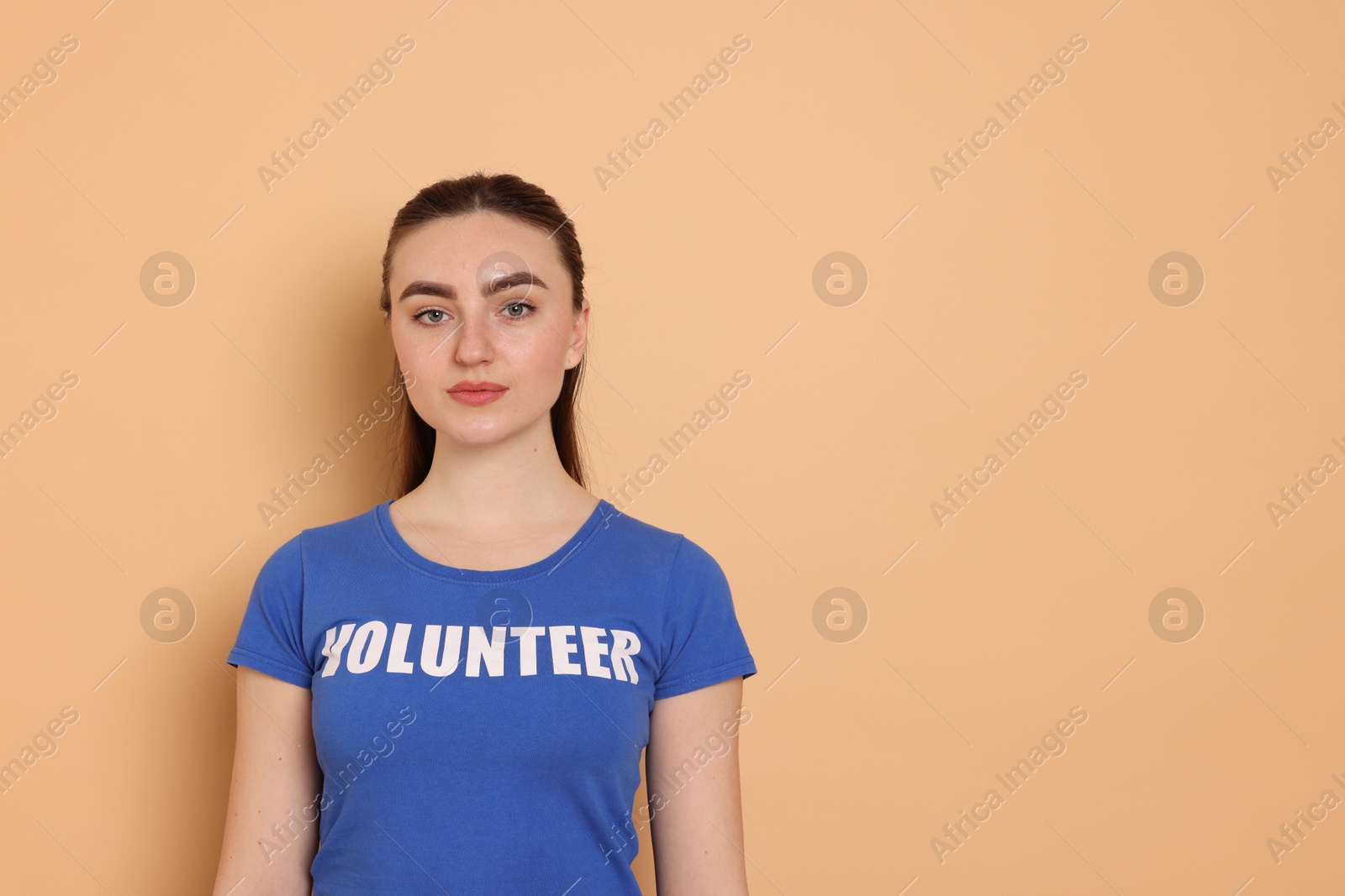 Photo of Portrait of woman in t-shirt with word Volunteer on beige background. Space for text