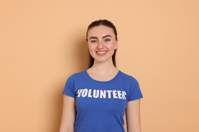 Photo of Portrait of smiling woman in t-shirt with word Volunteer on beige background