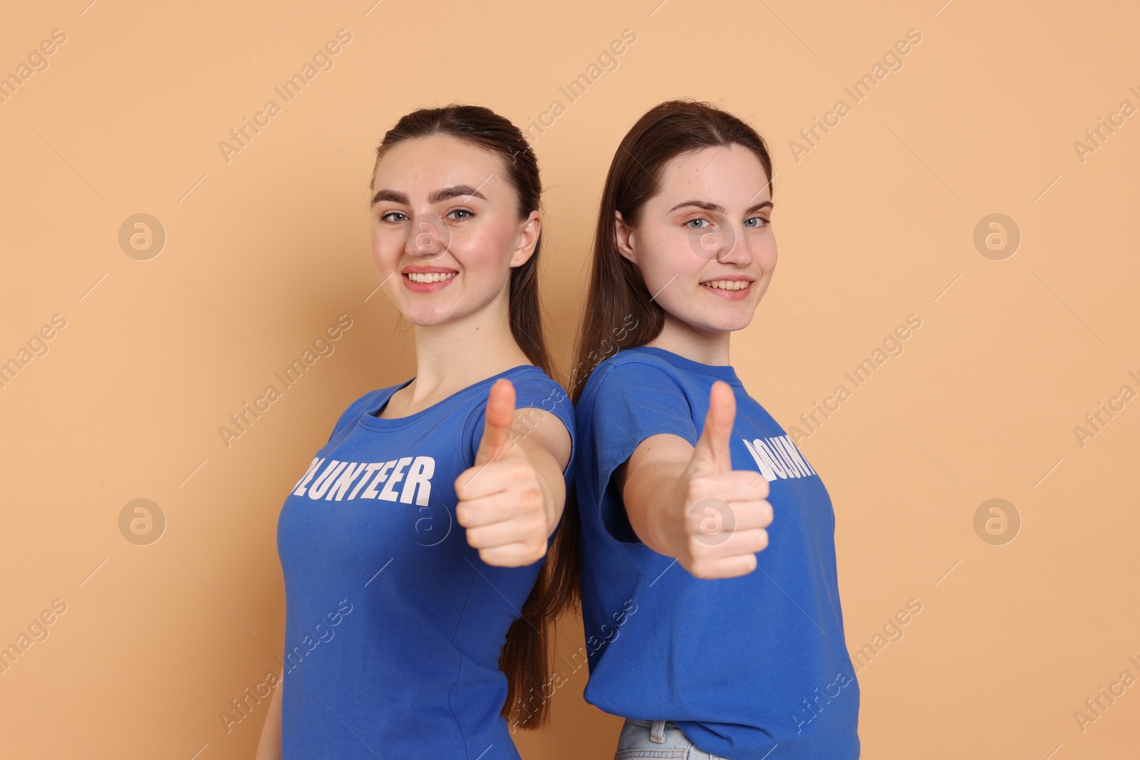 Photo of Portrait of smiling volunteers showing thumbs up on beige background