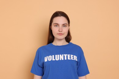 Photo of Portrait of woman in t-shirt with word Volunteer on beige background