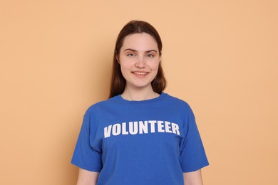 Photo of Portrait of smiling woman in t-shirt with word Volunteer on beige background