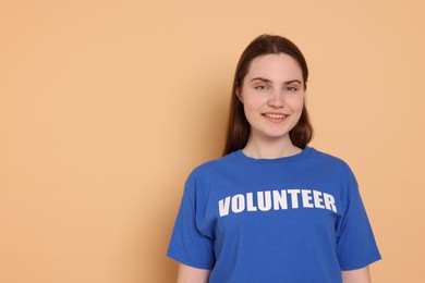 Photo of Portrait of smiling woman in t-shirt with word Volunteer on beige background. Space for text